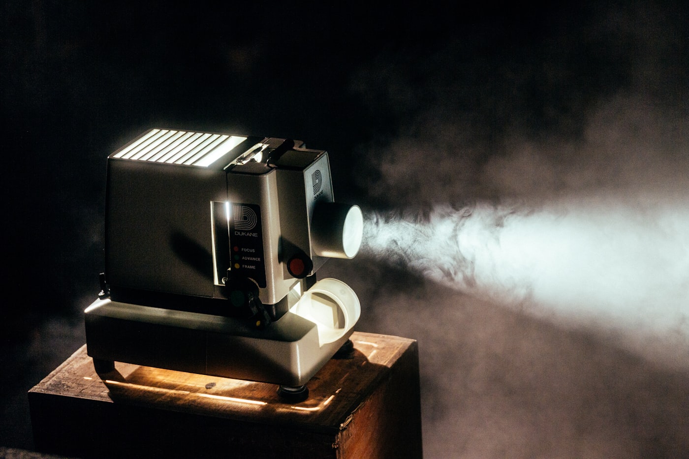 Vintage filmprojektor der kaster en lyskegle gennem røg i et mørkt rum